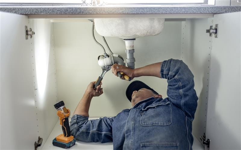 Plumber repairing pipes beneath a bathroom sink in Miami Gardens