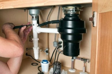 Plumber repairing a garbage disposal beneath a kitchen sink in Miami Gardens