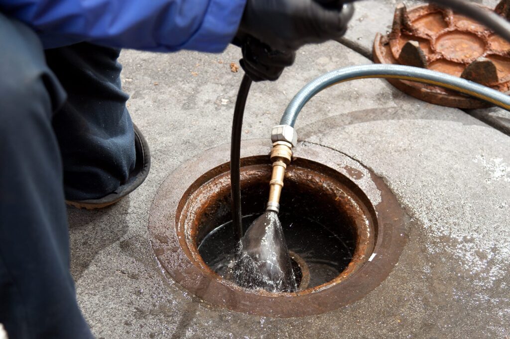 Plumber hydro jetting a sewer line through a manhole in Miami Gardens