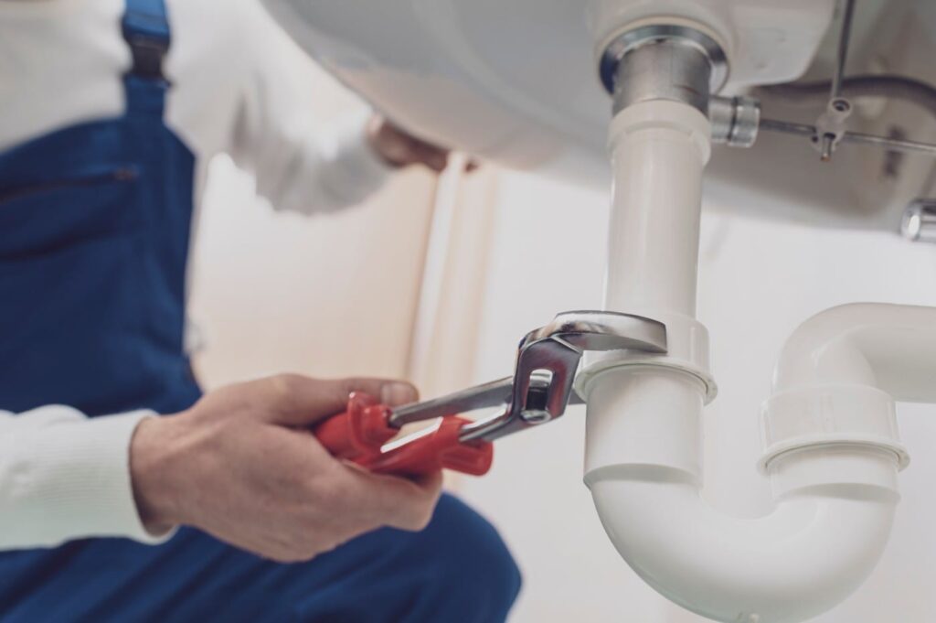 Plumber repairing a white drain pipe beneath a sink in Miami Gardens