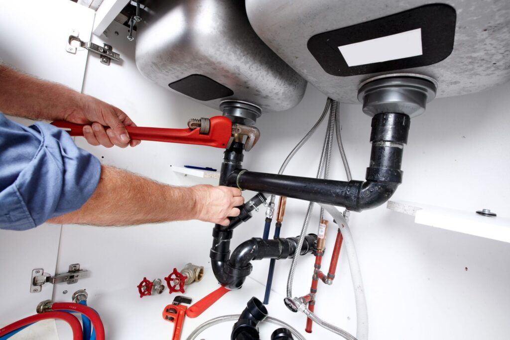 Plumber repairing drain pipes beneath a kitchen sink in Miami Gardens